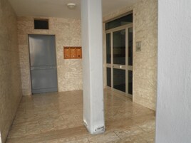 Un pasillo con piso de mármol, una puerta gris y una puerta de cristal con marco de metal.