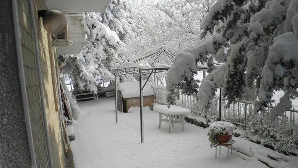 Un patio cubierto de nieve con un quiosco, una silla blanca y una mesa.