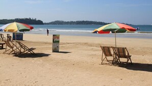 Une plage avec deux parasols colorés, des chaises longues en bois et un panneau indiquant un centre de bien-être.