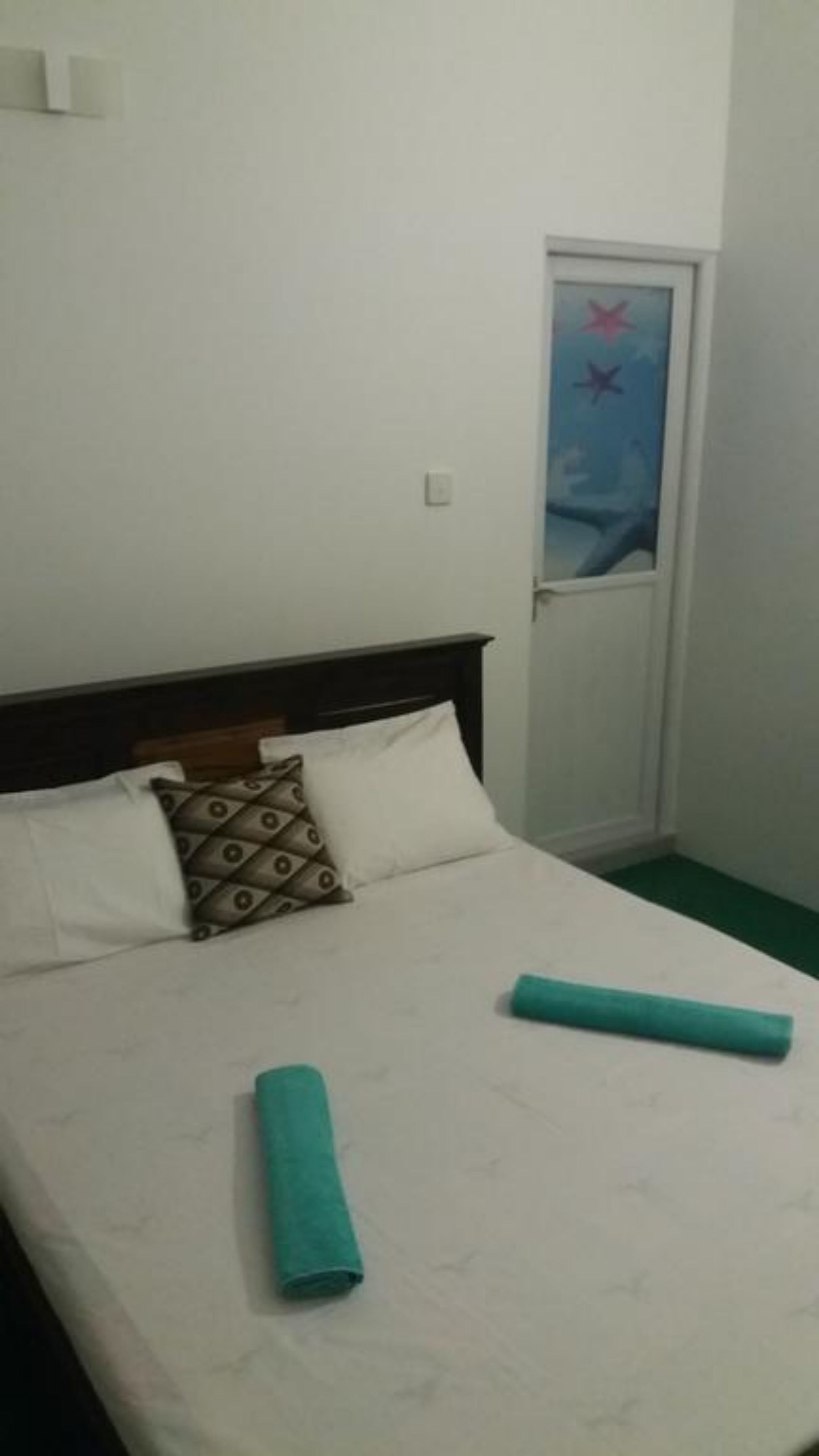 A bed with white bedding, a patterned pillow, and a teal rolled towel.