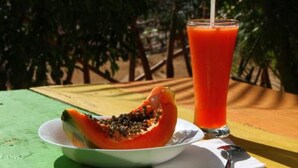 Une table avec un verre de jus et un fruit coupé en deux, vraisemblablement une papaye, posés sur une nappe verte.