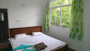 Un lit bien fait, avec du linge de lit blanc et un coussin à motifs, une tête de lit en bois et une fenêtre ornée de rideaux en bambou vert.