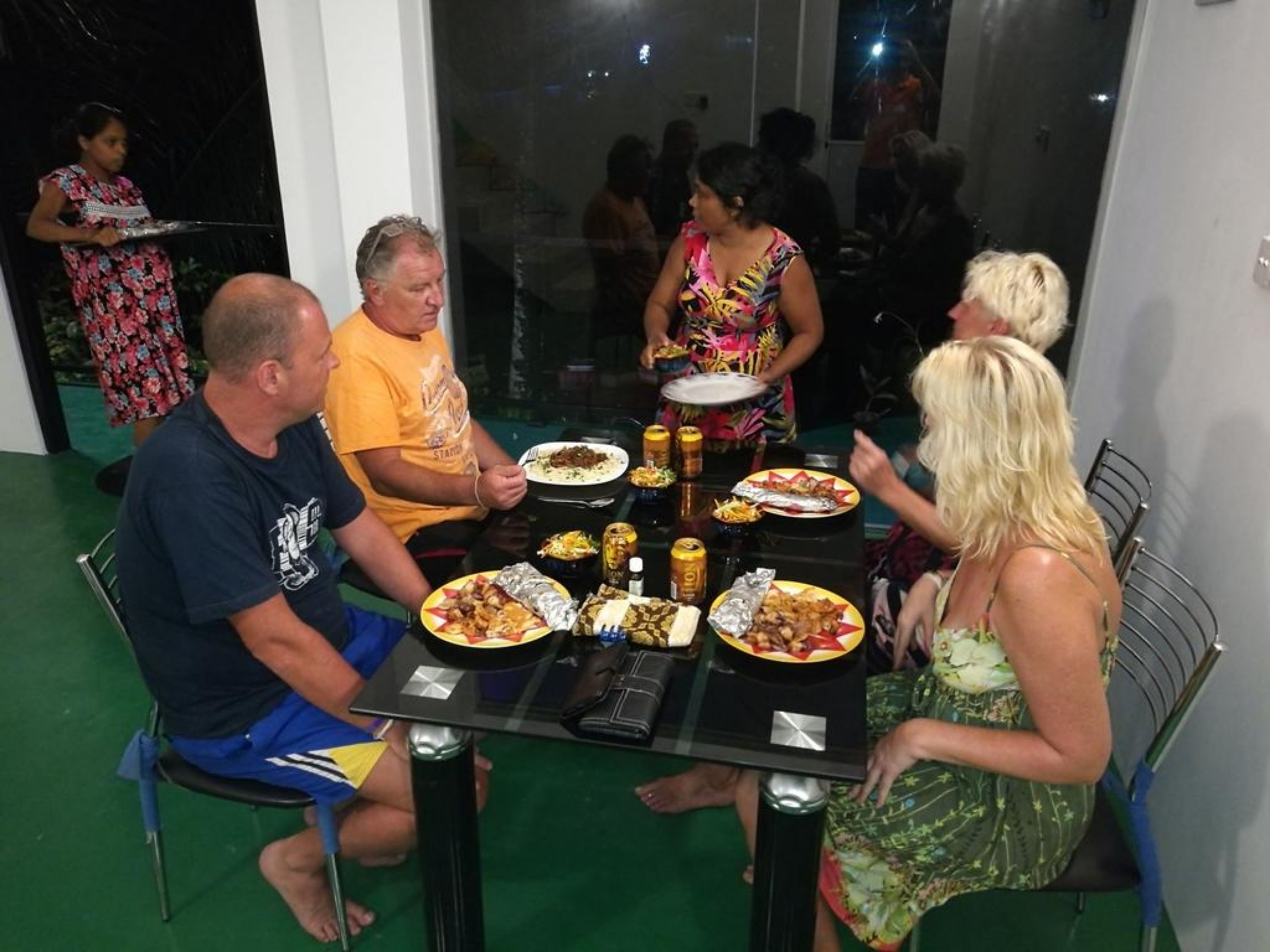 A group of people dining at an outdoor table with various dishes and drinks.