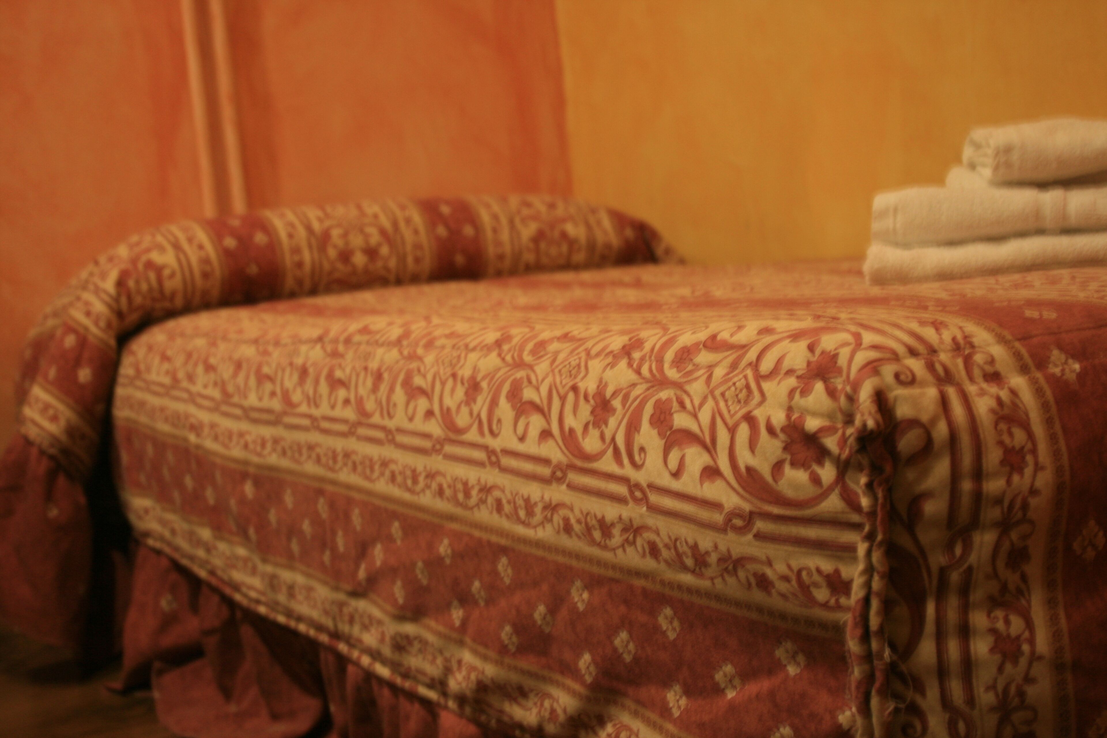 Una cama con una colcha estampada y almohadas, además de una pila de toallas dobladas a un lado.