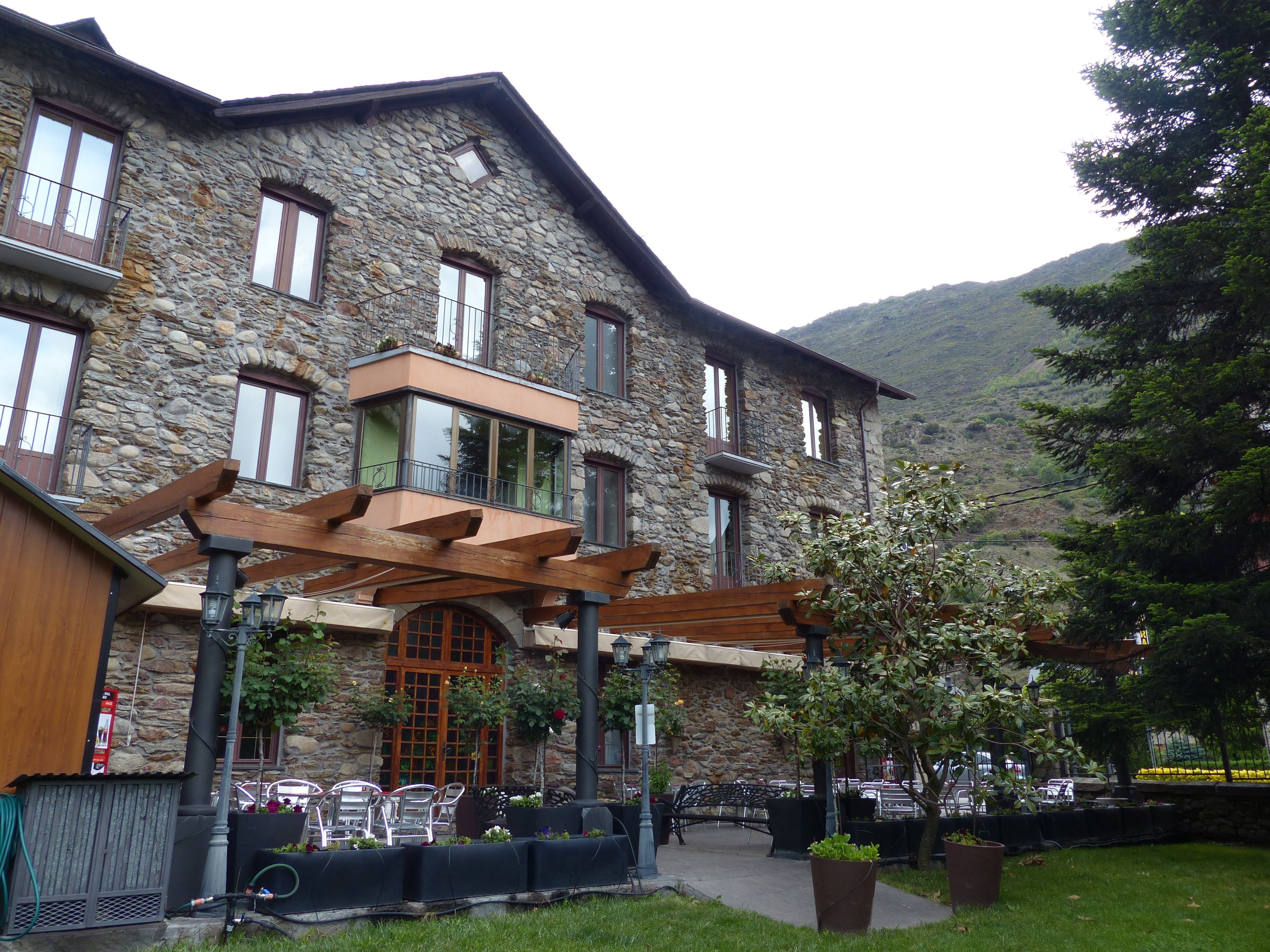 A stone building with a balcony, outdoor seating, and a mountain backdrop.