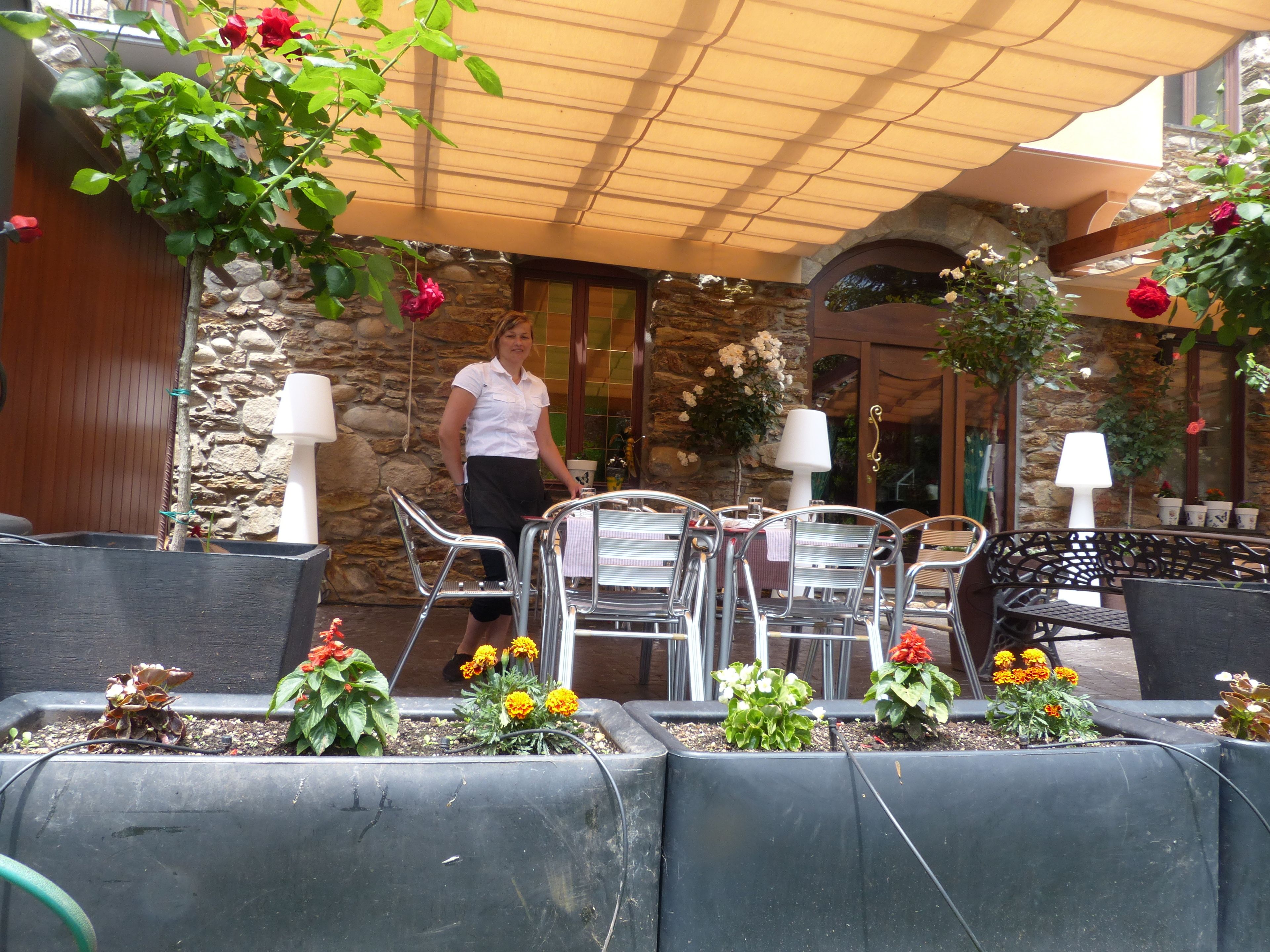 An outdoor patio area with metal chairs and tables, stone walls, and potted plants.
