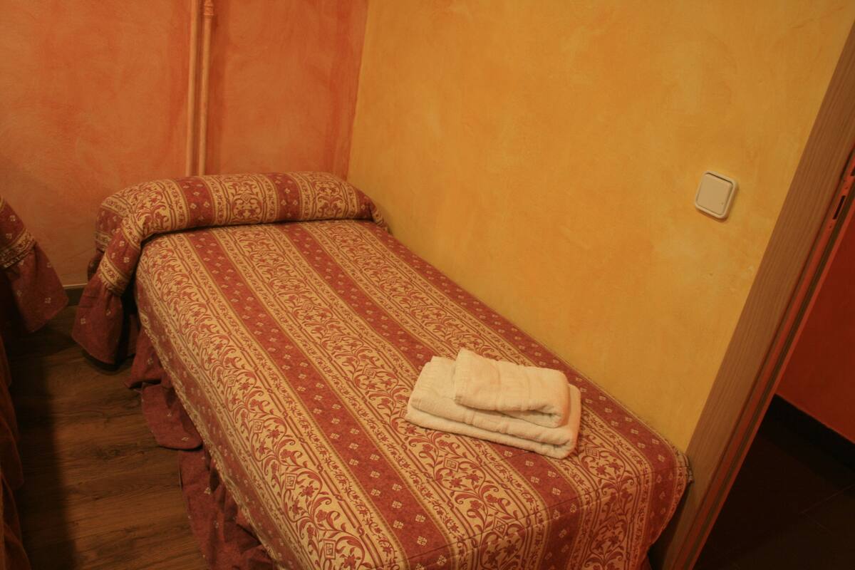 A small, single-bed room with a patterned bedspread and a folded towel on the bed.