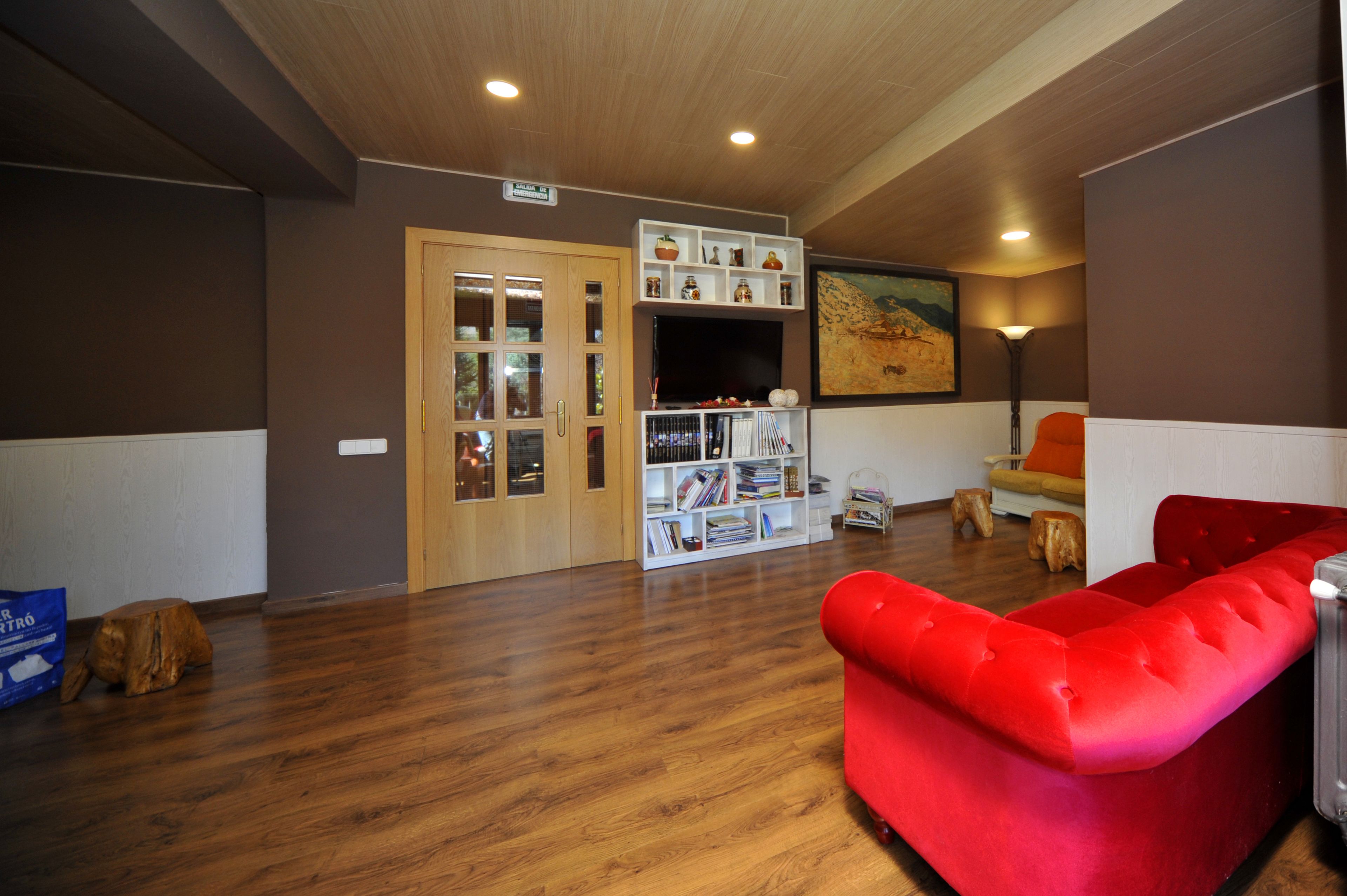 A room with a red sofa, wooden flooring, a bookshelf, and a door with glass panels.