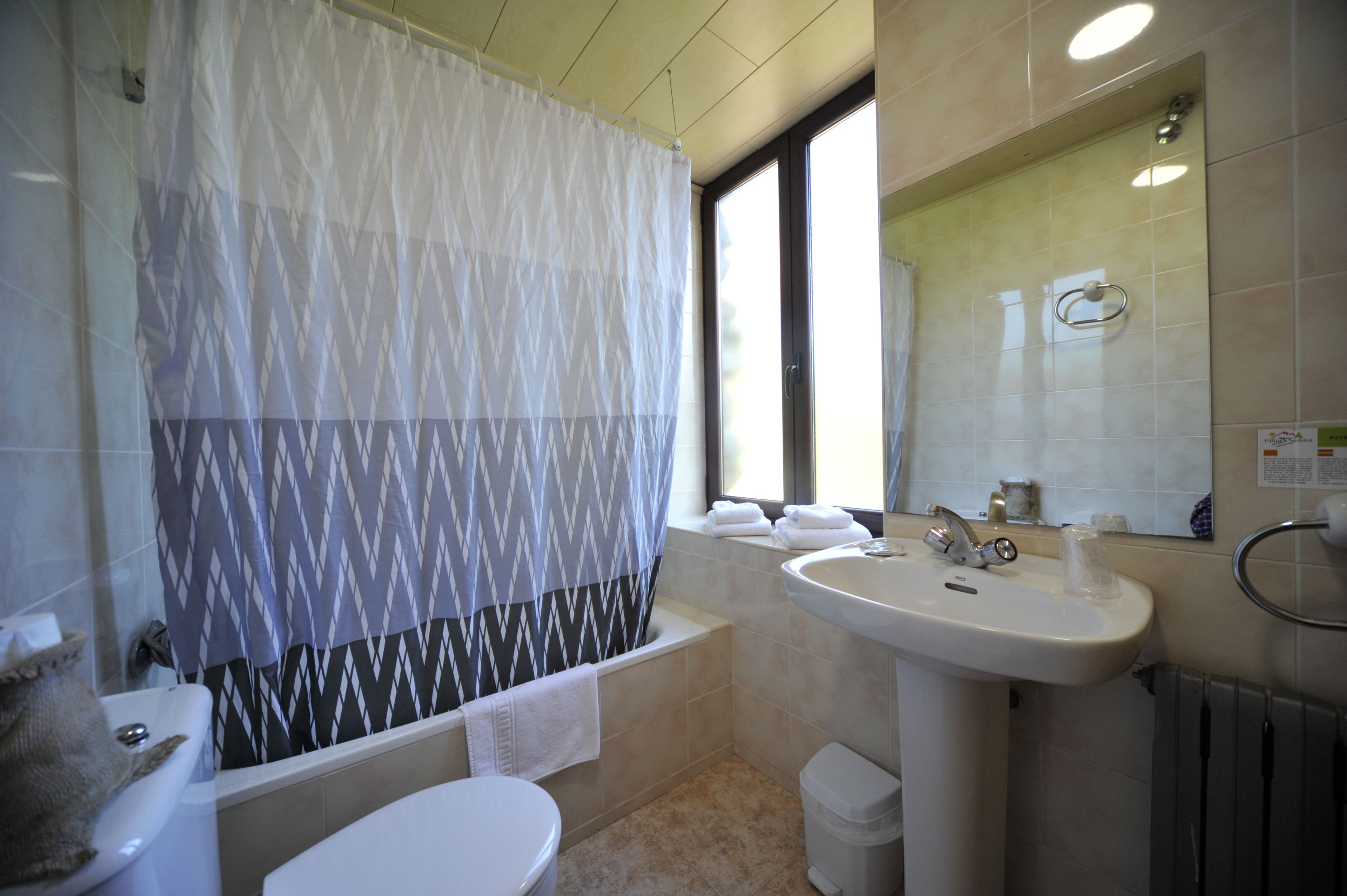 Un baño con bañera, inodoro, lavabo y ventana con cortina.