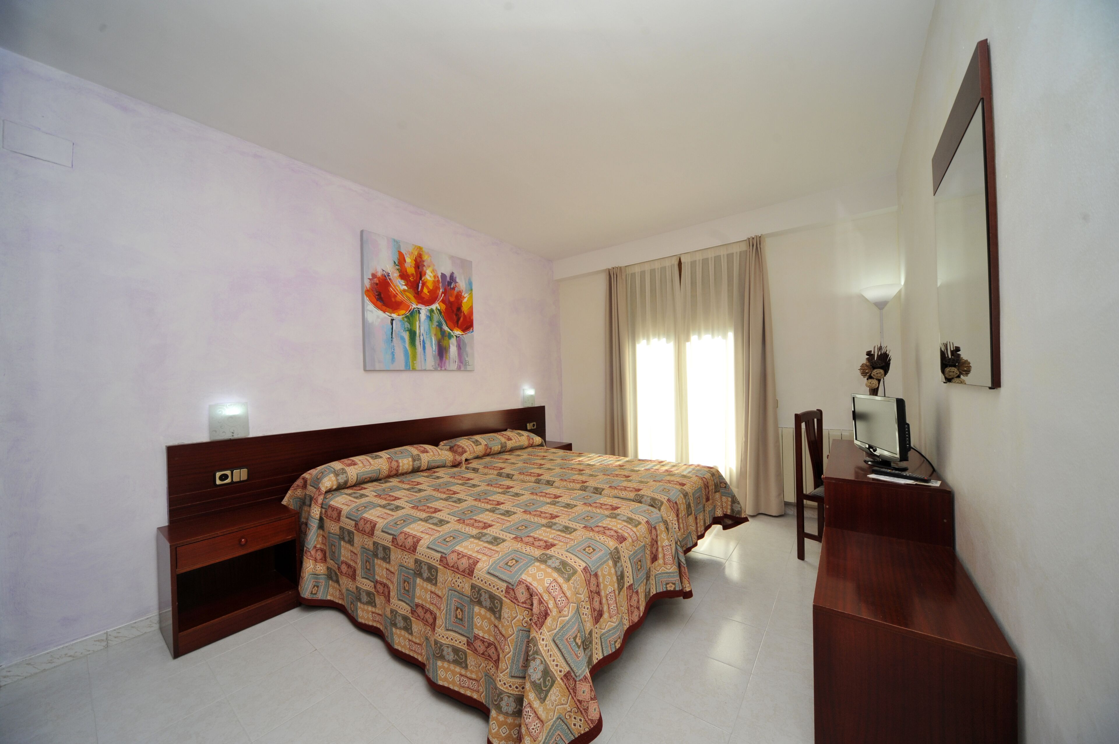 A bedroom with a bed, a desk, a chair, a painting, and a window with curtains.