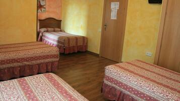 A room with three beds, wooden flooring, a wooden door, and a wall-mounted TV.