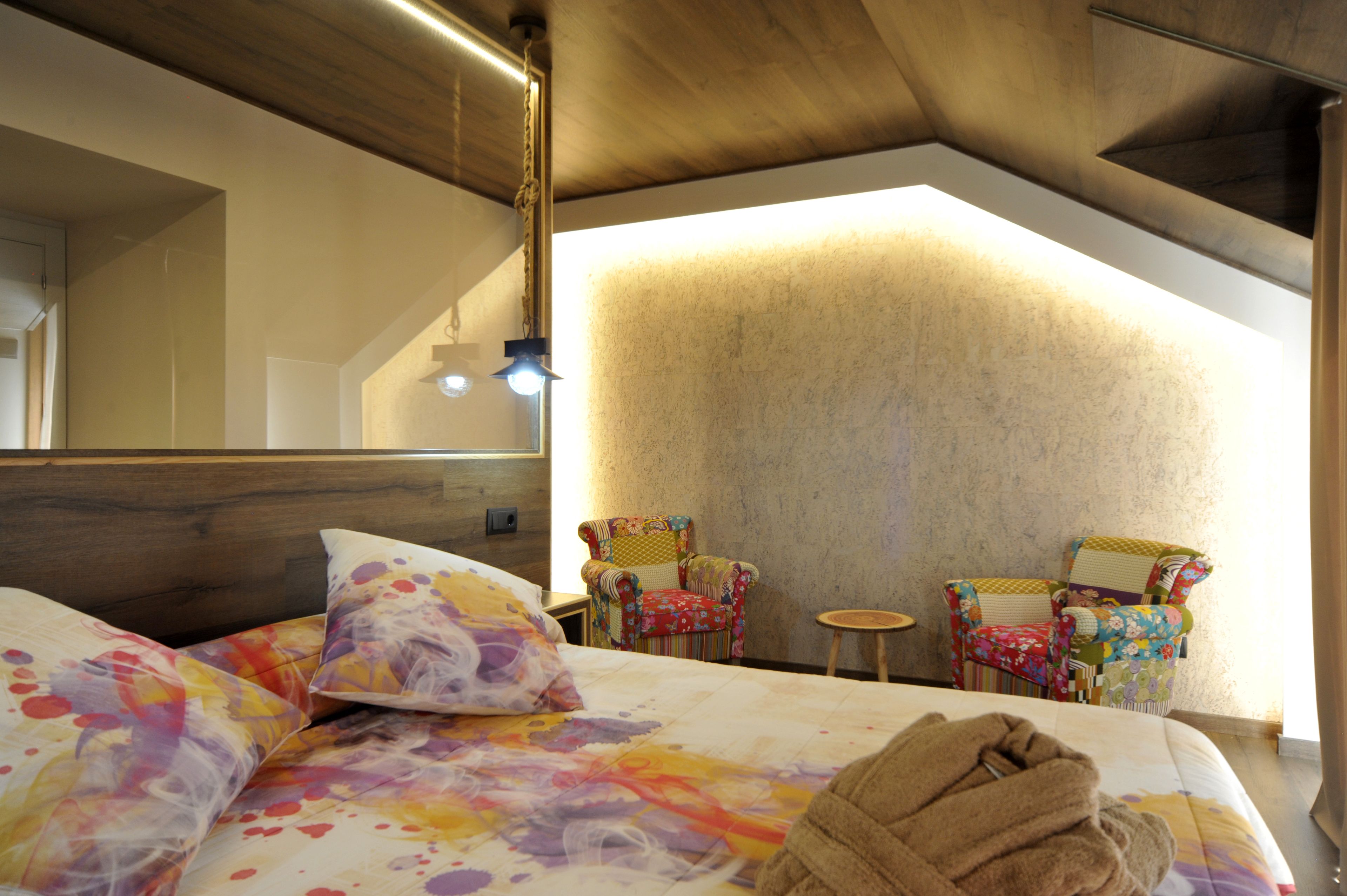Une chambre à coucher avec un lit, deux chaises, une petite table et un grand miroir.