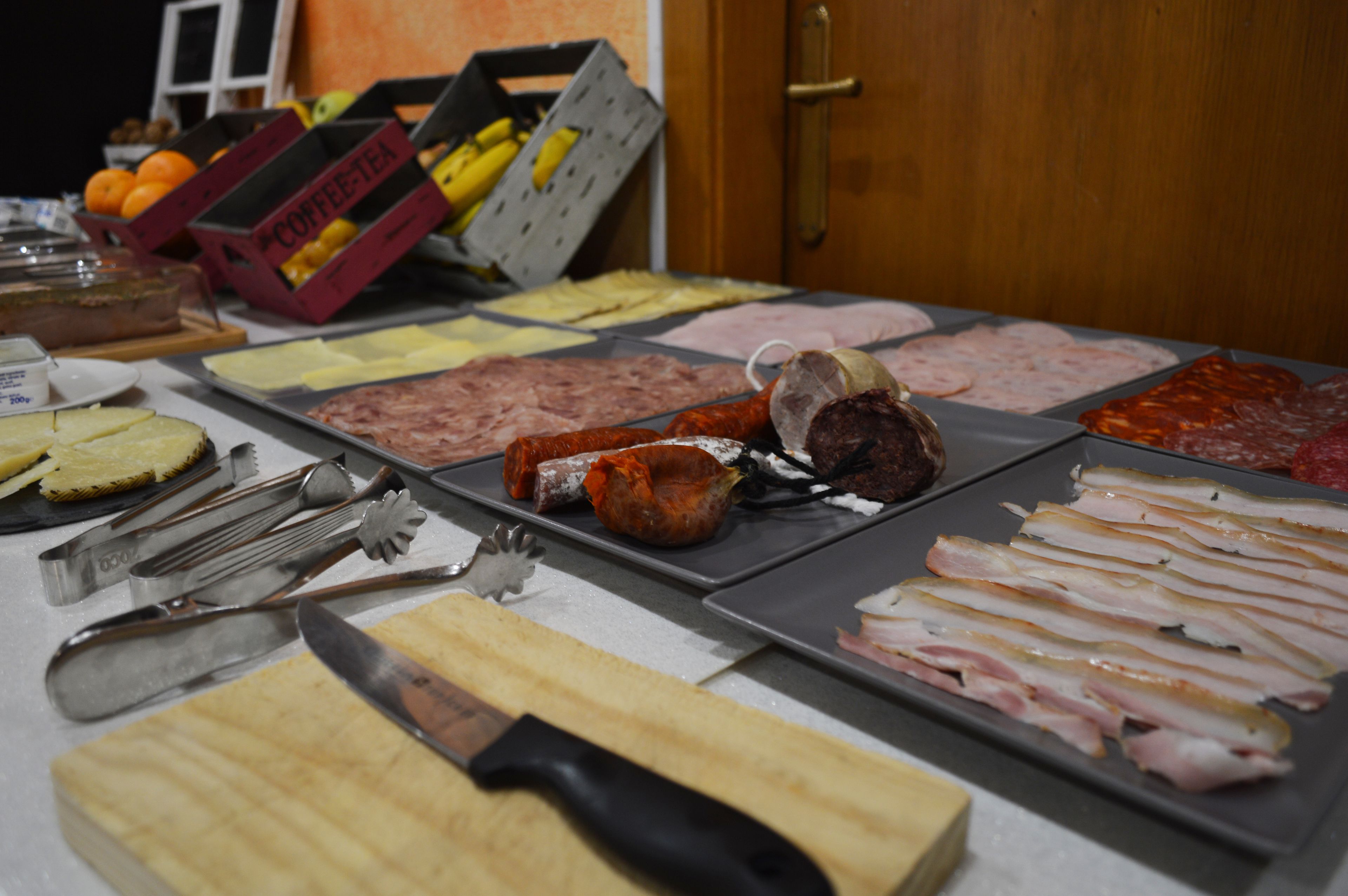 Variedad de carnes y quesos sobre una mesa, junto con cuchillos y una tabla de cortar.
