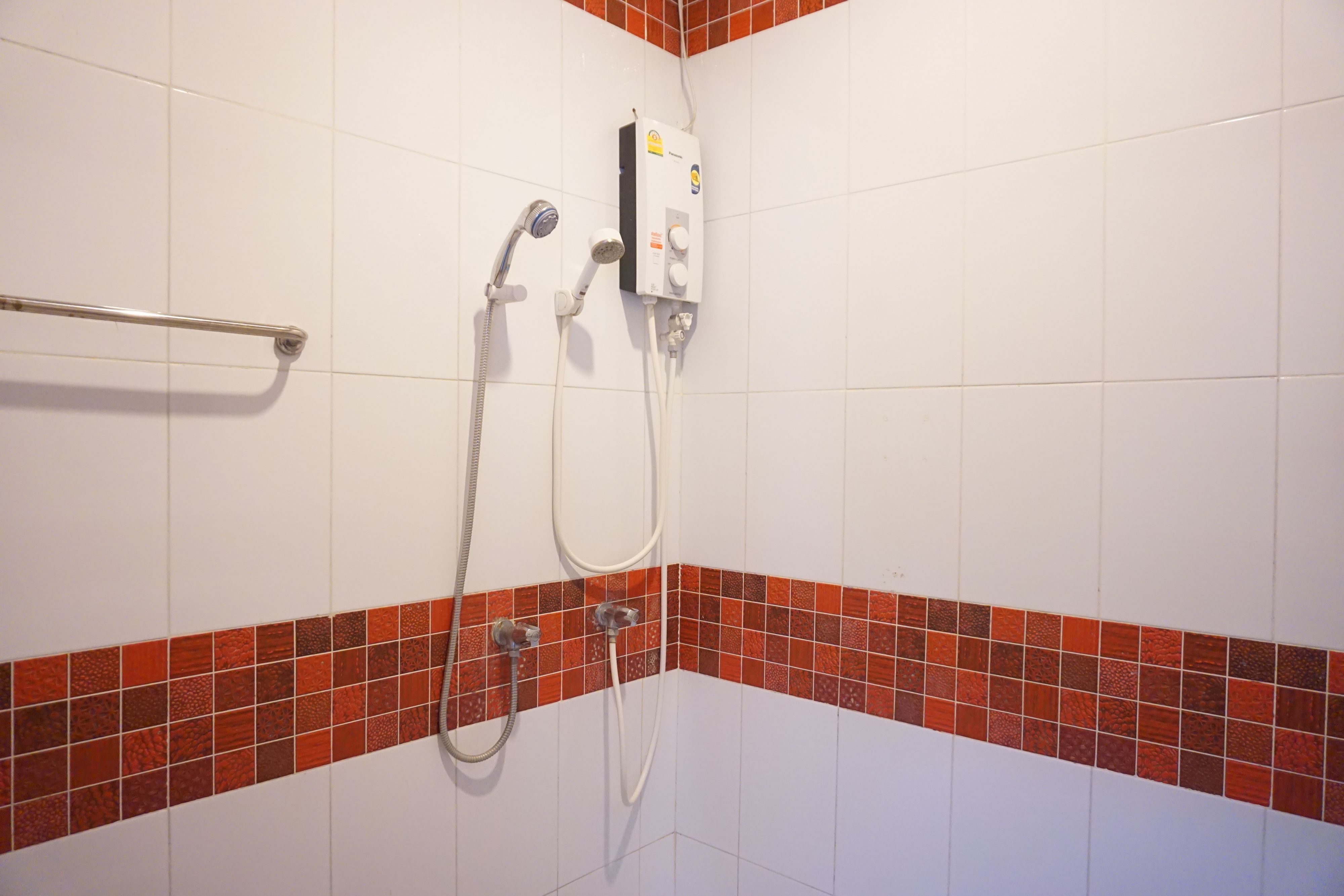 Un área de ducha con cabezal de ducha de mano y panel de control en la pared.