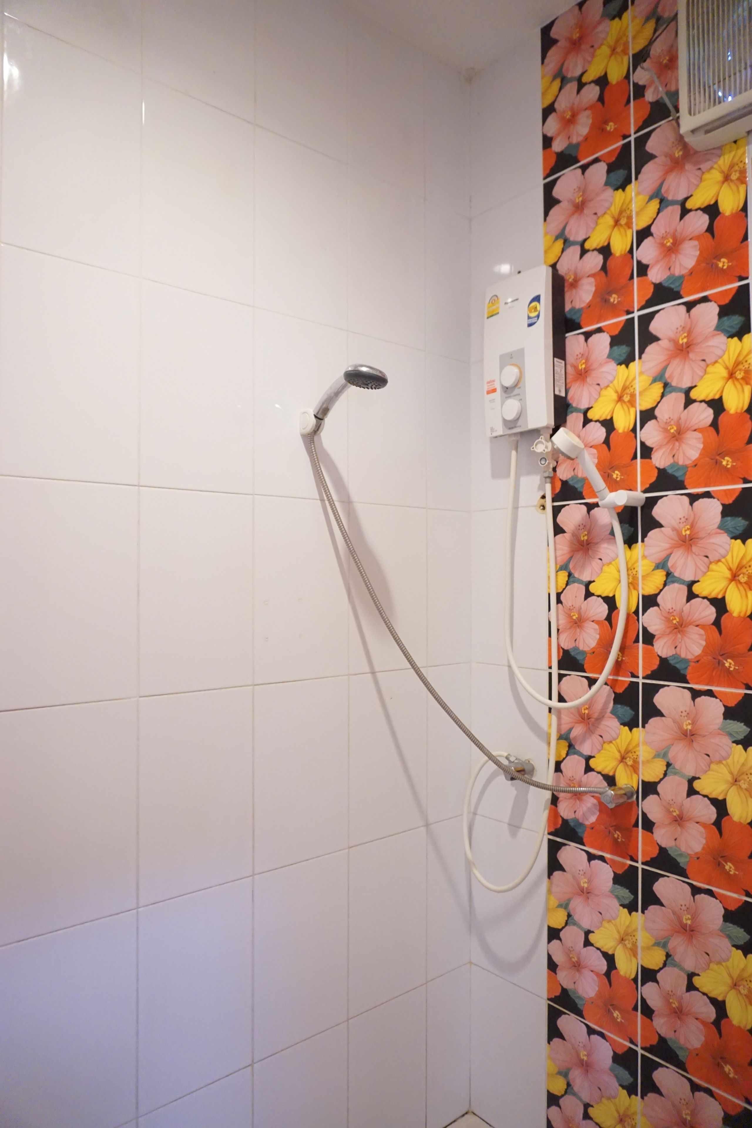 A shower with a floral tile design on the wall and a white tiled floor.