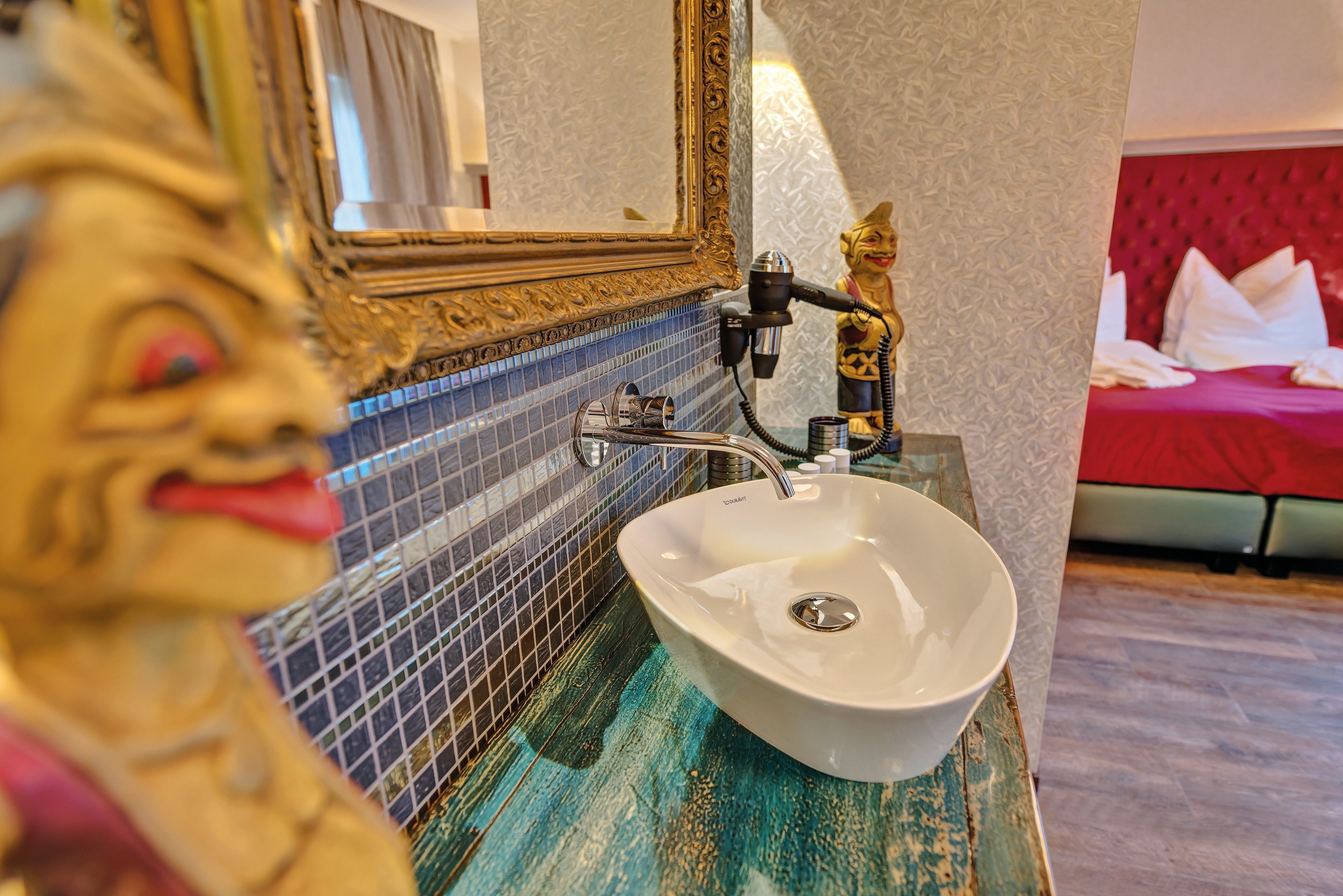 Een badkamer met een wit wastafelmeubel, een spiegel met een sierlijk frame en een beeldje.