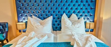 A hotel room with a tufted headboard, two white pillows, a blue bedspread, and two white towels.