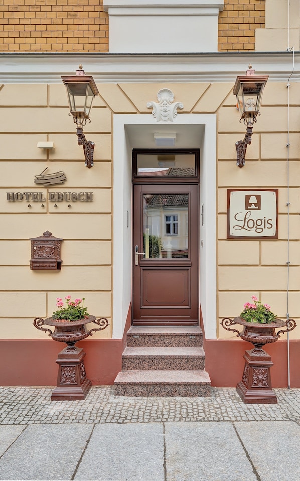 A hotel entrance with a brown door, a sign reading "HOTEL EBUSCH", and a "Logis" sign above the door.
