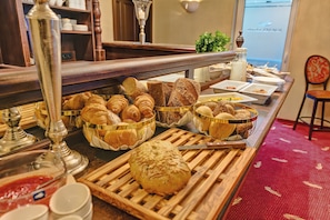 A buffet with various breads and pastries, including croissants and baguettes, arranged on a wooden table.