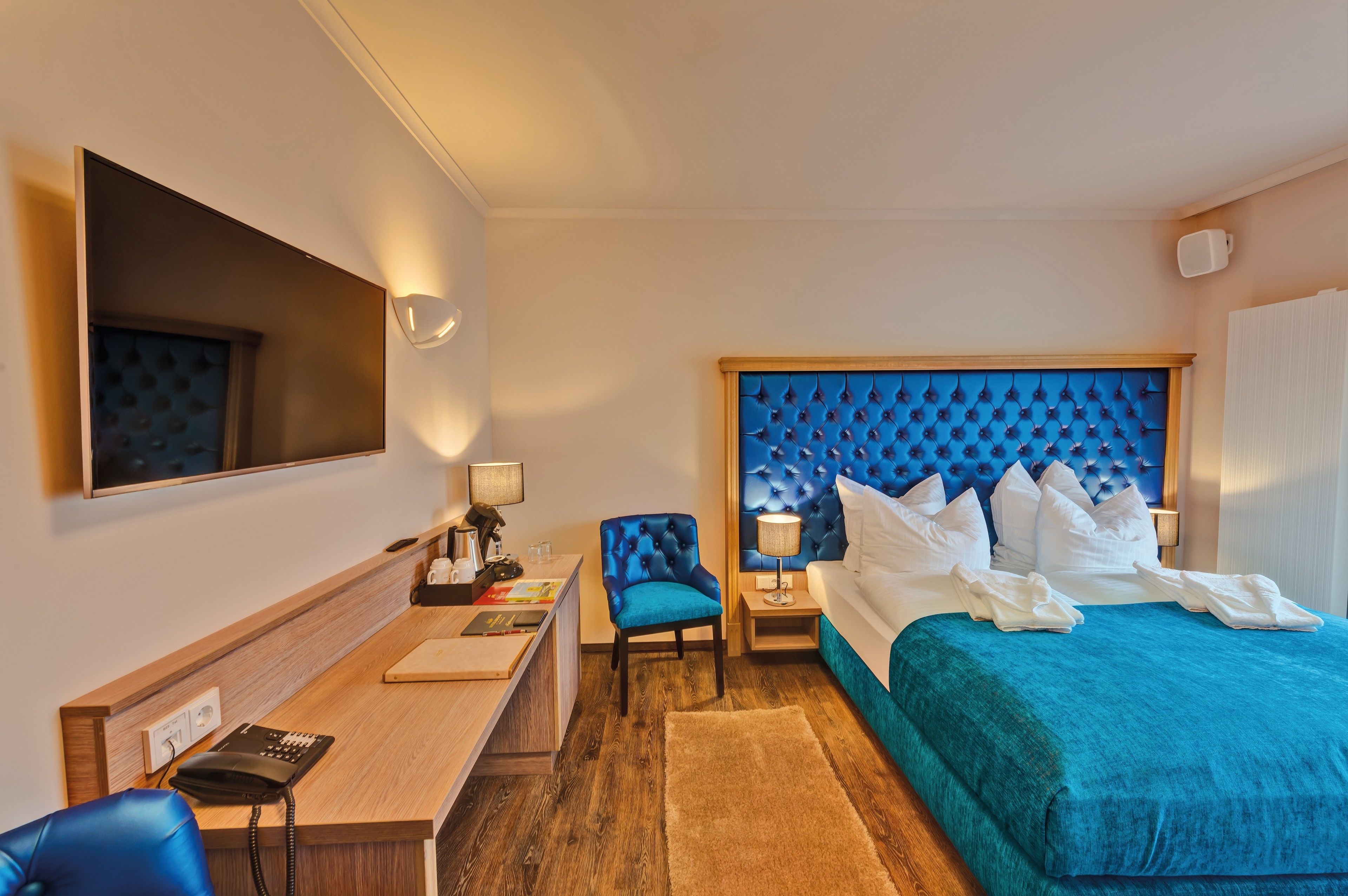 Una habitación de hotel con una cama grande, un escritorio con teléfono, una silla y un televisor en la pared.