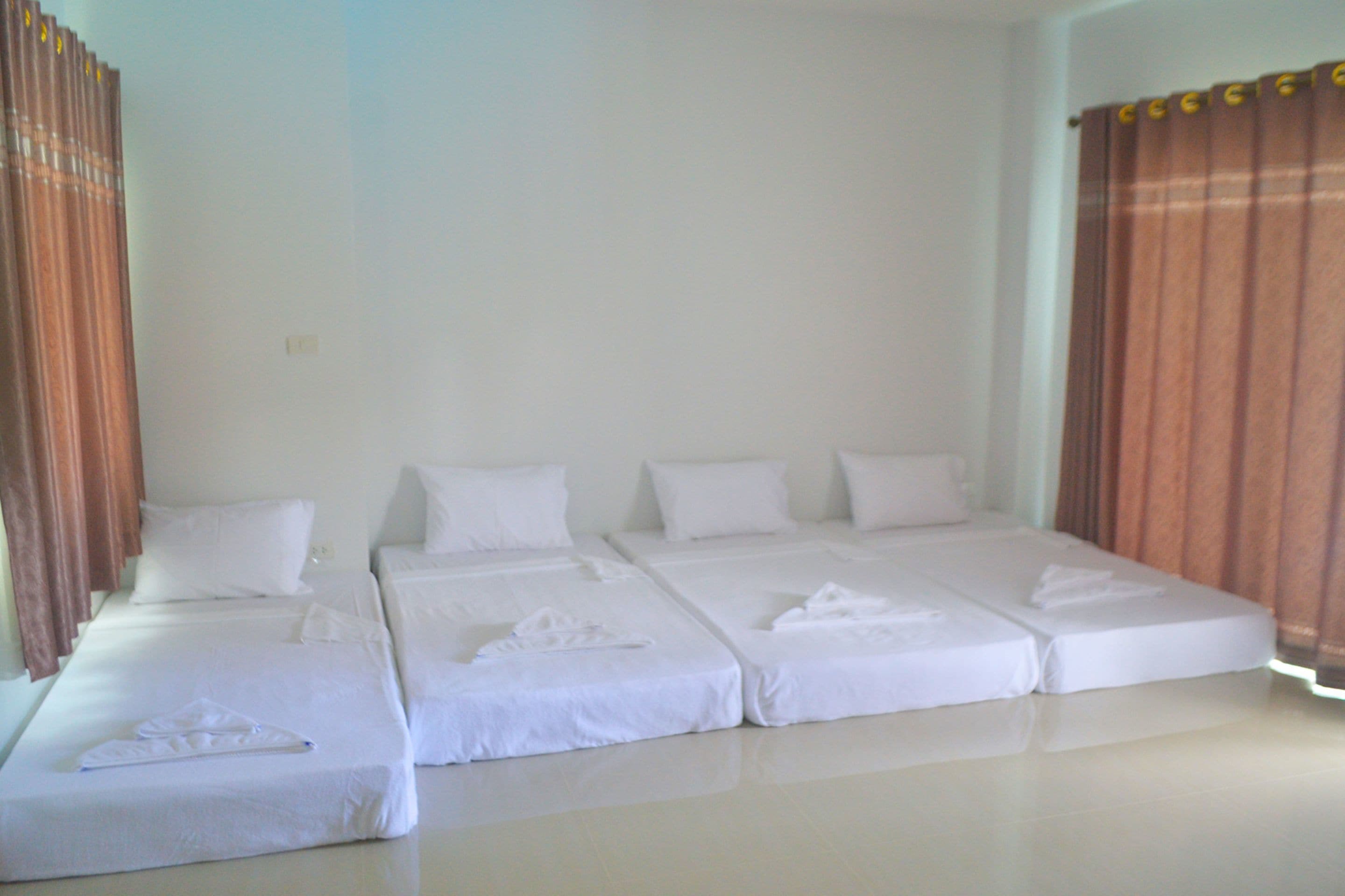 A hotel room with three single beds arranged in a row, white bedding, and curtains on both sides.