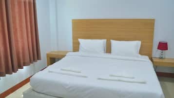 A neatly made bed with white linens, two pillows, and a wooden headboard. There are two bedside tables with lamps, one red and one white.