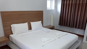 Un letto rifatto con lenzuola bianche, una testiera in legno, un comodino e una finestra con tende.