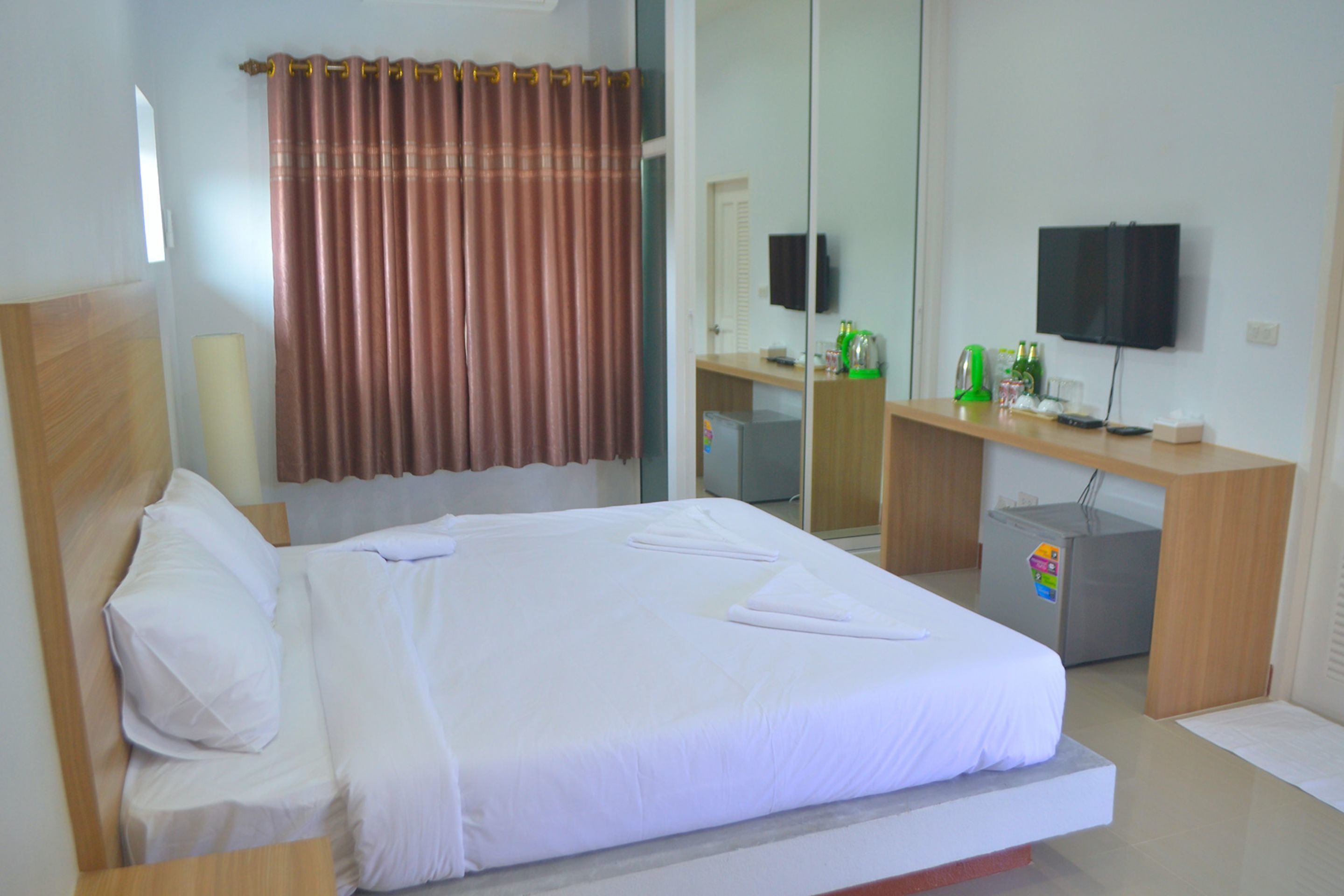 Habitación de hotel con cama, escritorio, espejo, televisor y refrigerador.