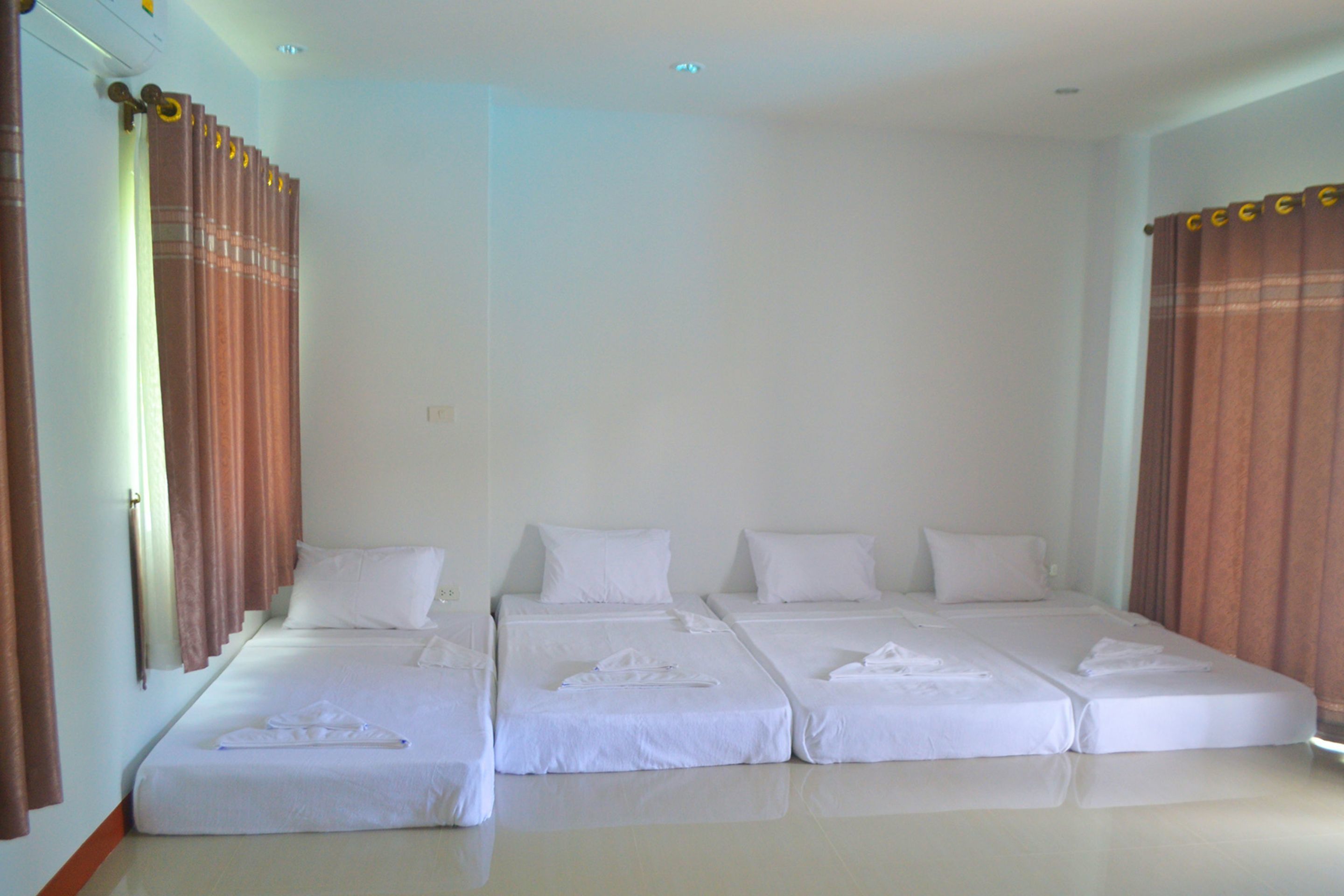 A hotel room with four single beds, each with white linens and pillows, arranged in a row.