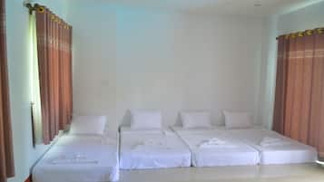 A hotel room with four single beds, each with white linens and pillows, arranged in a row.