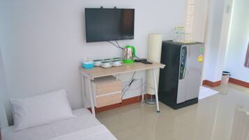 A hotel room with a bed, a desk with a television, a refrigerator, and a trash bin.