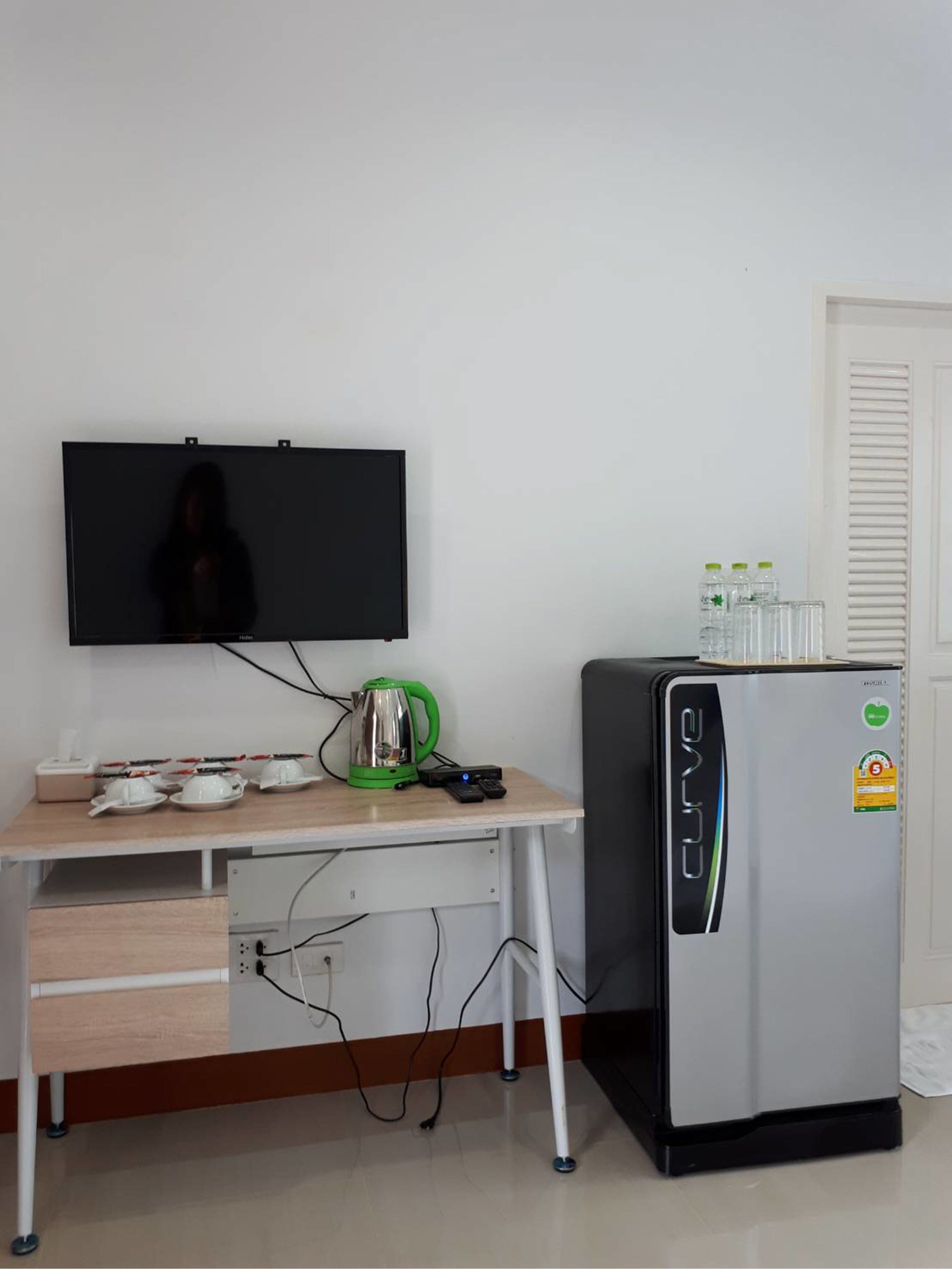 Una kitchenette con una televisión, un refrigerador, un hervidor y una cafetera sobre una mesa de madera.