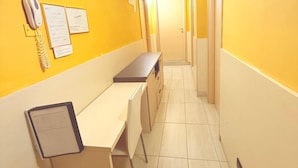 A narrow hallway with yellow walls, a white ceiling, and a desk with a chair. - Hola Roma (Rome)