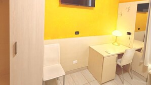 A hotel room with a yellow wall, a flat-screen TV mounted above a desk, a wardrobe, a chair, and a bedside table. - Hola Roma (Rome)