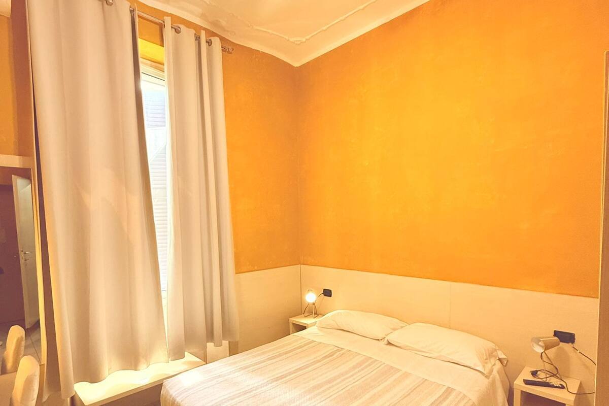 A hotel room with a bed, bedside tables, a ceiling fan, and a window with curtains.