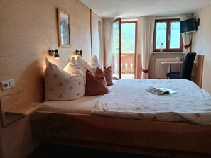A bedroom with a bed, pillows, a desk, a chair, a TV, and a window.
