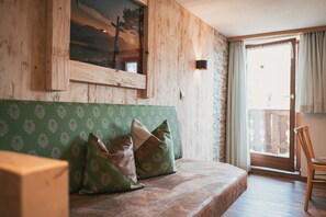 Quarto com painéis de madeira, um sofá verde com padrão, uma cadeira de madeira e uma janela grande com vista.