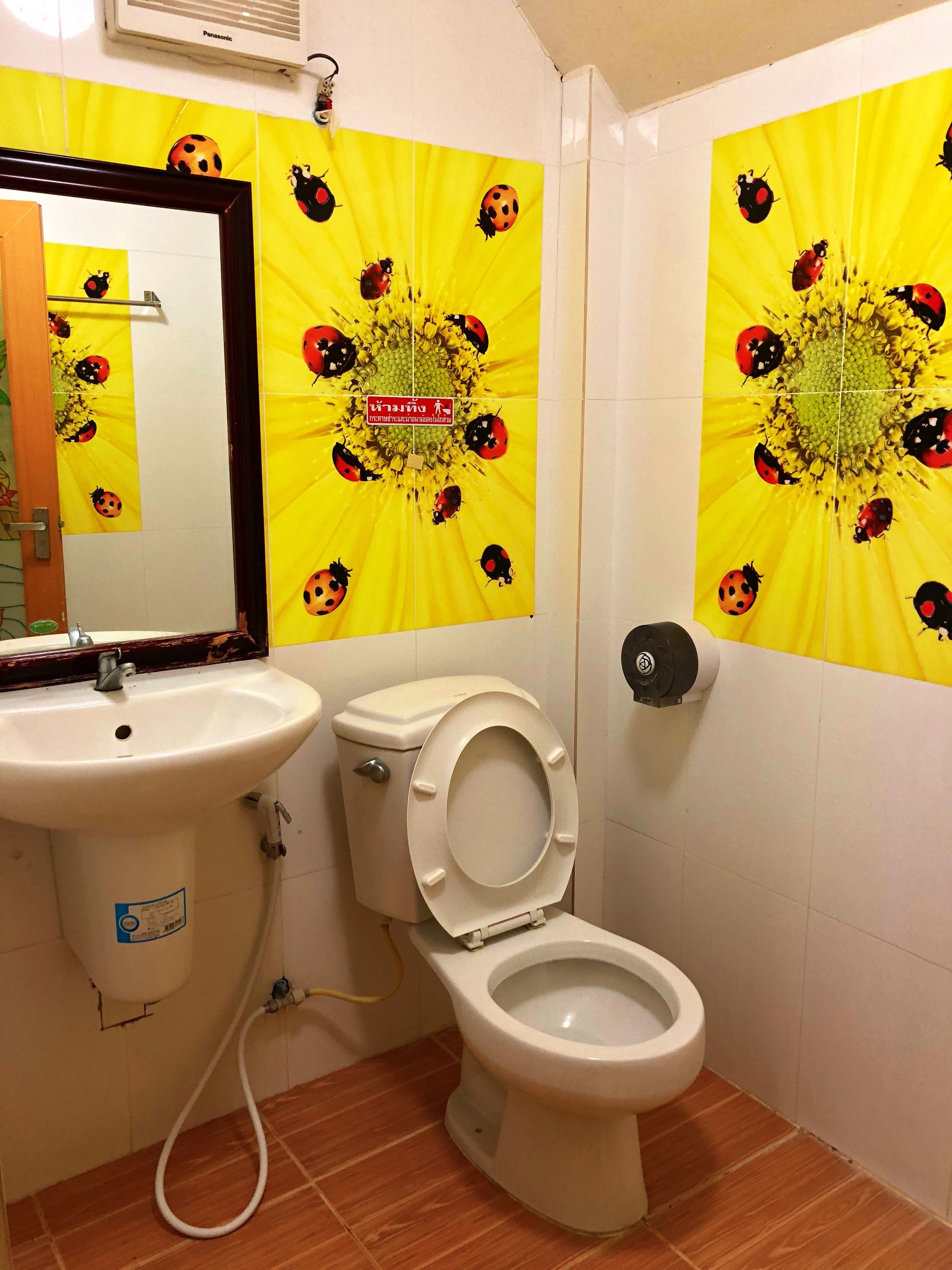 A bathroom with a sink, toilet, and mirror. The walls are decorated with yellow tiles featuring ladybug designs.