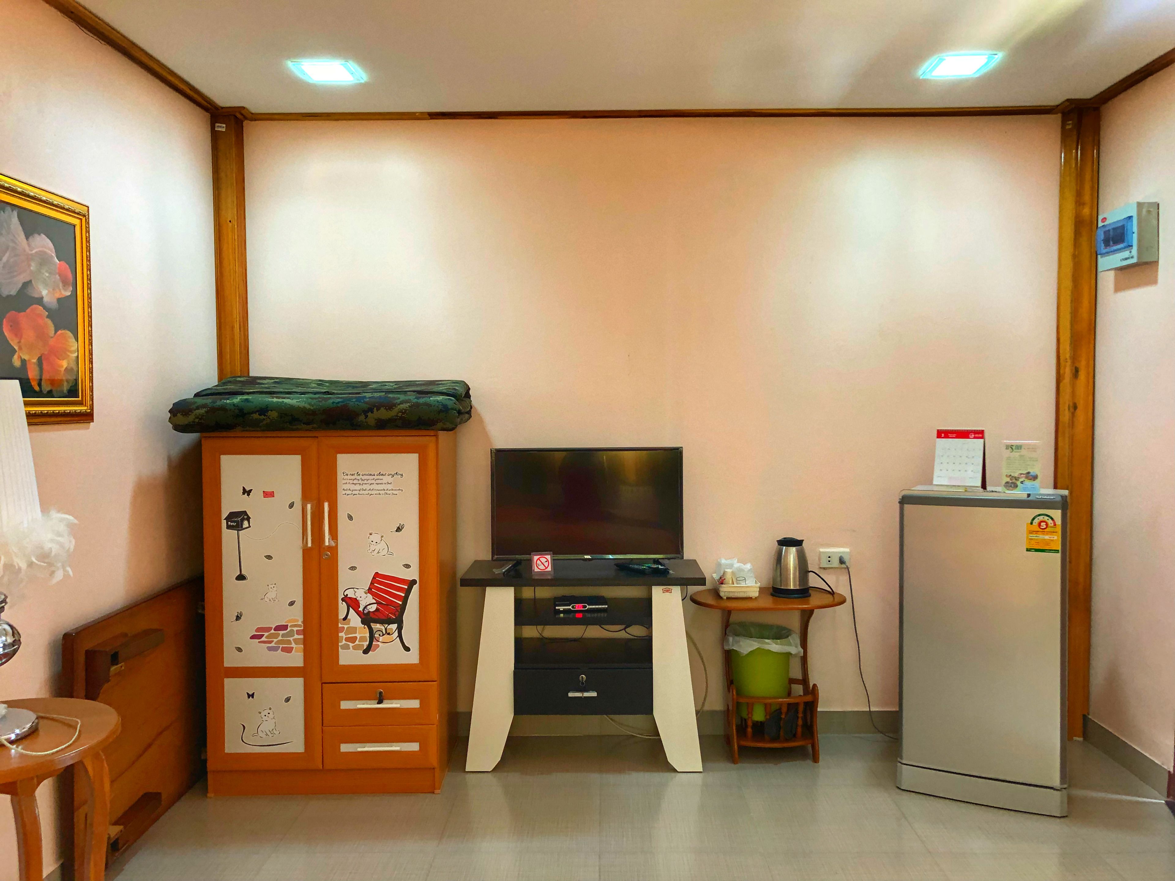 A small room with a wooden cabinet, a television, a small table with a trash bin, and a refrigerator.