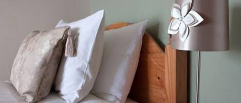 A neatly made bed with white and patterned pillows, a wooden headboard, and a modern floor lamp with a metallic base and a flower design on the lampshade.