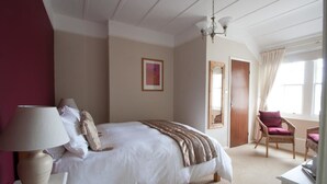 A bedroom with a bed, a bedside lamp, a chair, a door, and a window. - Gyves Guest House (Eastbourne)
