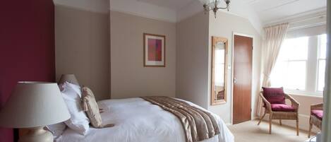 A bedroom with a bed, a bedside lamp, a chair, a door, and a window.
