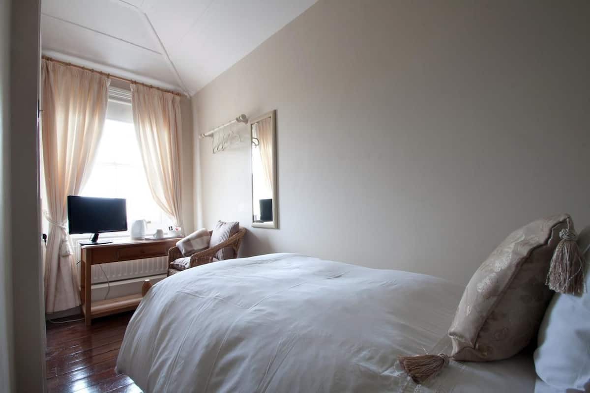 Ein Schlafzimmer mit einem großen Bett, einem Schreibtisch mit Computer und einem Fenster mit Vorhängen.