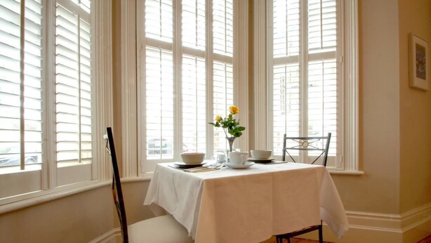 A dining area with a table set for two, a vase with yellow flowers, and a chair. - Gyves Guest House (Eastbourne)