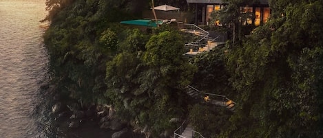 A luxurious house with a private dock, surrounded by lush greenery and overlooking a body of water.