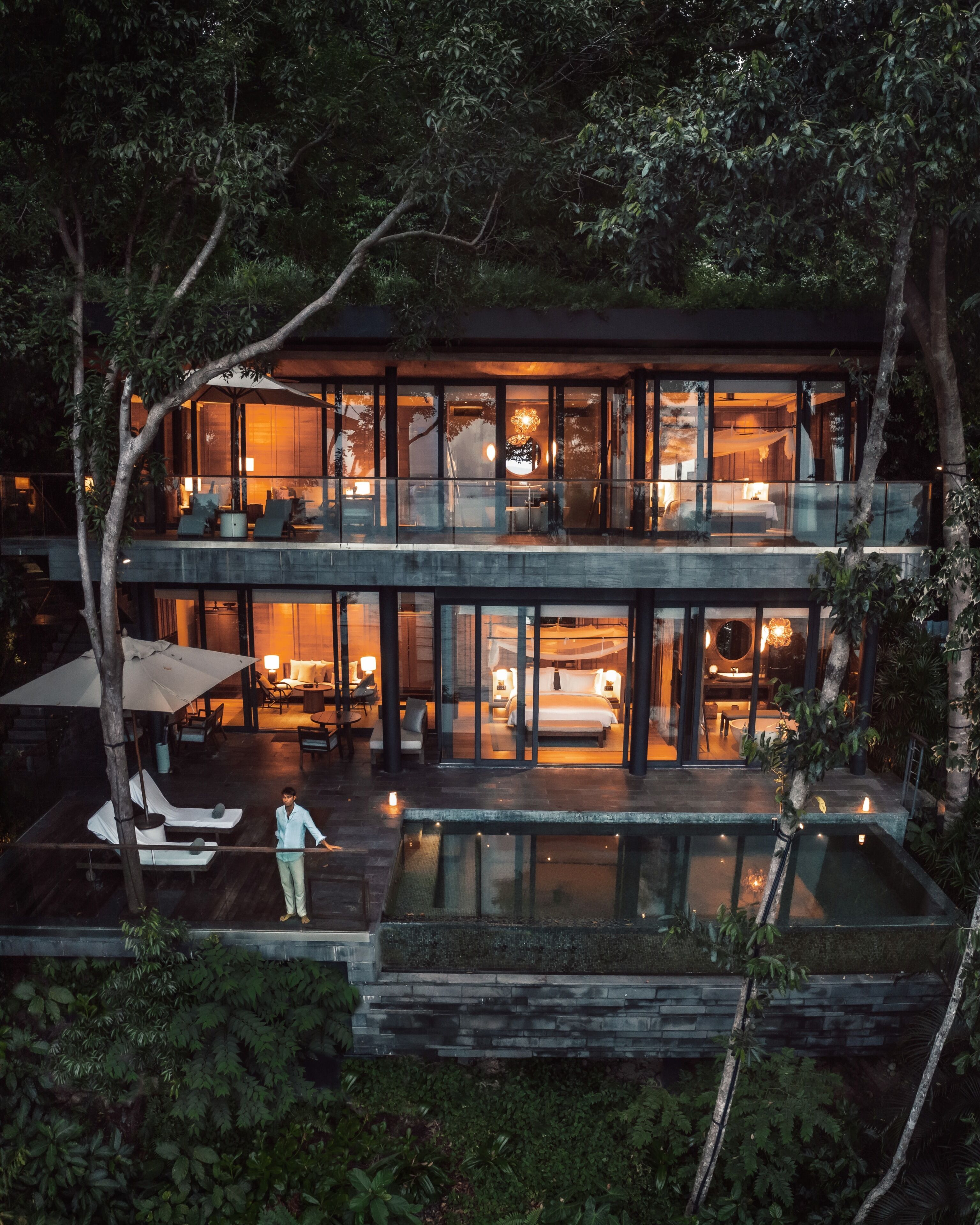A modern two-story house with a glass facade, a pool, and outdoor seating.