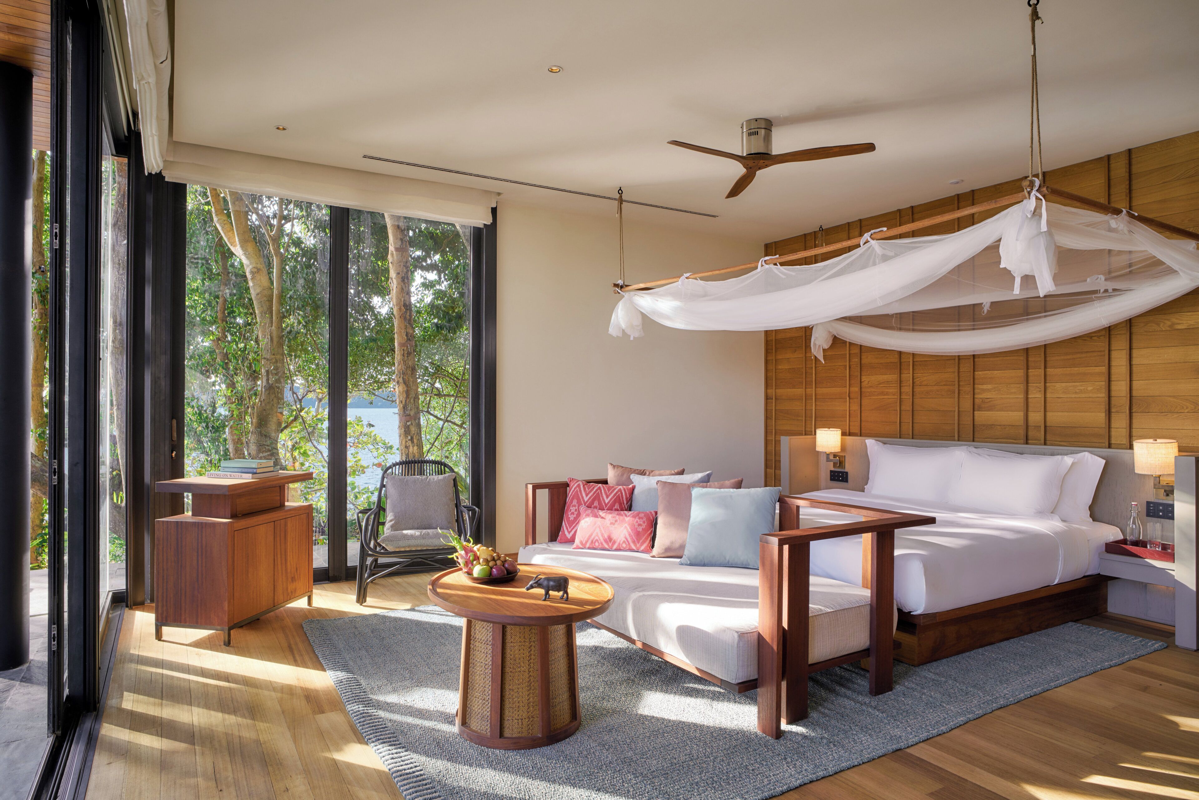 A modern hotel room with a bed, bedside tables, a sofa, a coffee table, and a ceiling fan.