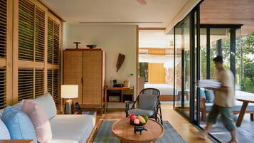 A modern hotel room with a sofa, a round wooden table with fruit, a chair, and a large wardrobe.