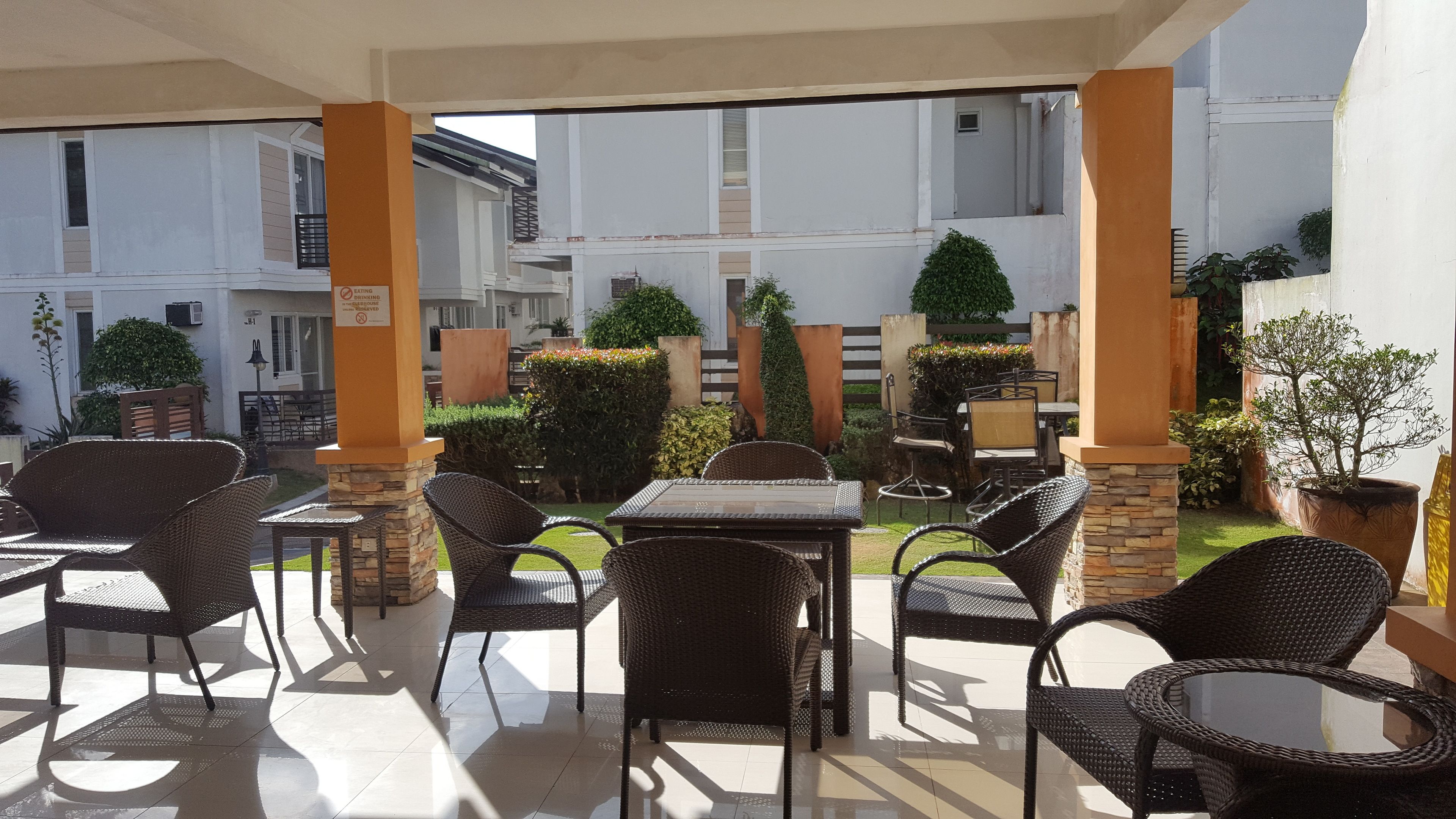 Un espace extérieur aménagé en terrasse, avec des meubles en osier, un sol carrelé et une vue sur la façade du bâtiment.