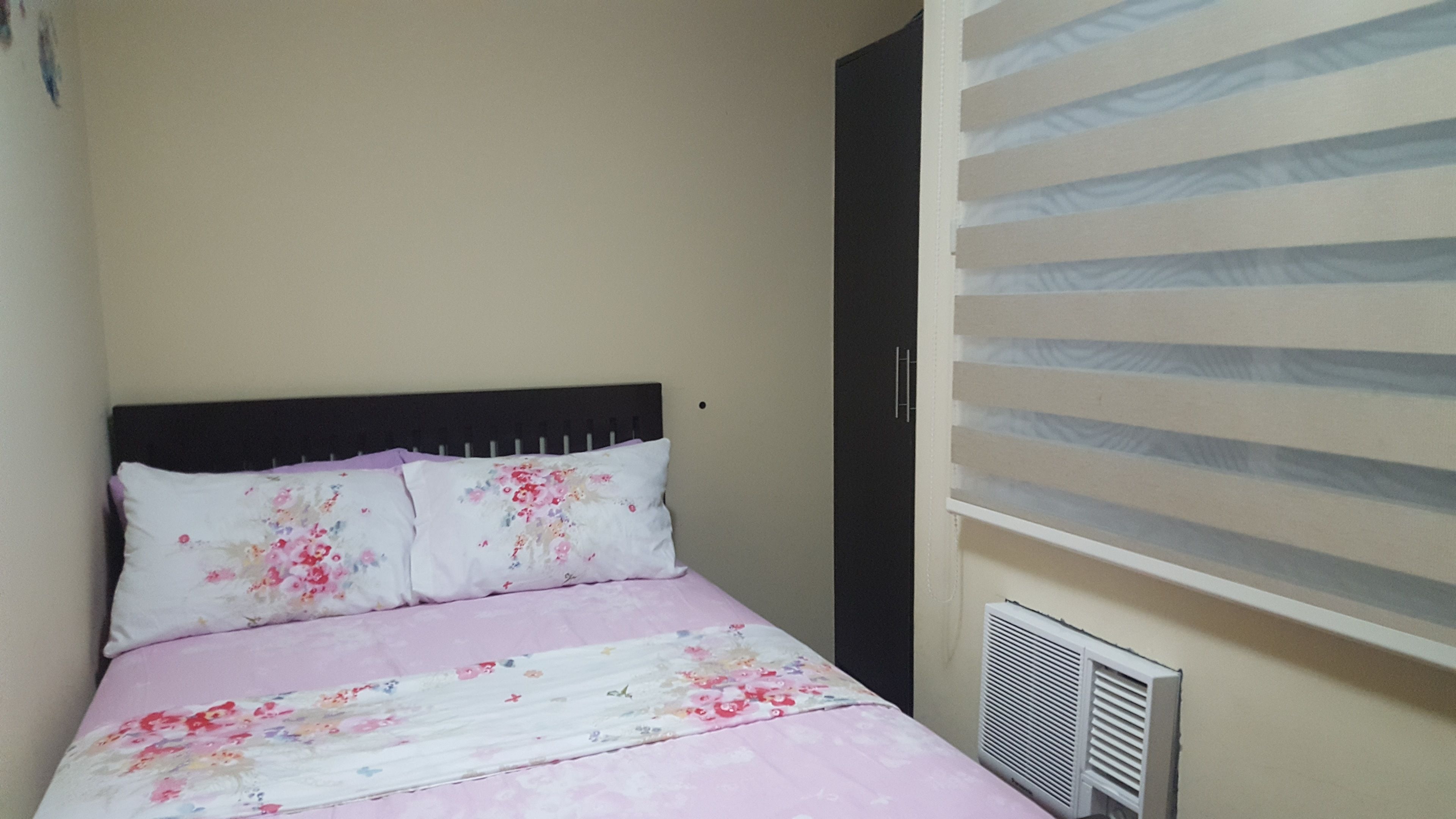 A bedroom with a bed, a window with blinds, and a radiator.